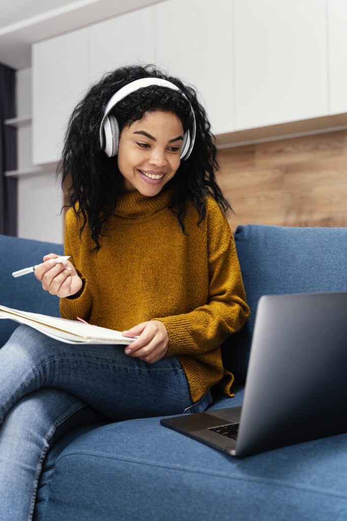 Young woman studying with headphones and laptop, smiling.