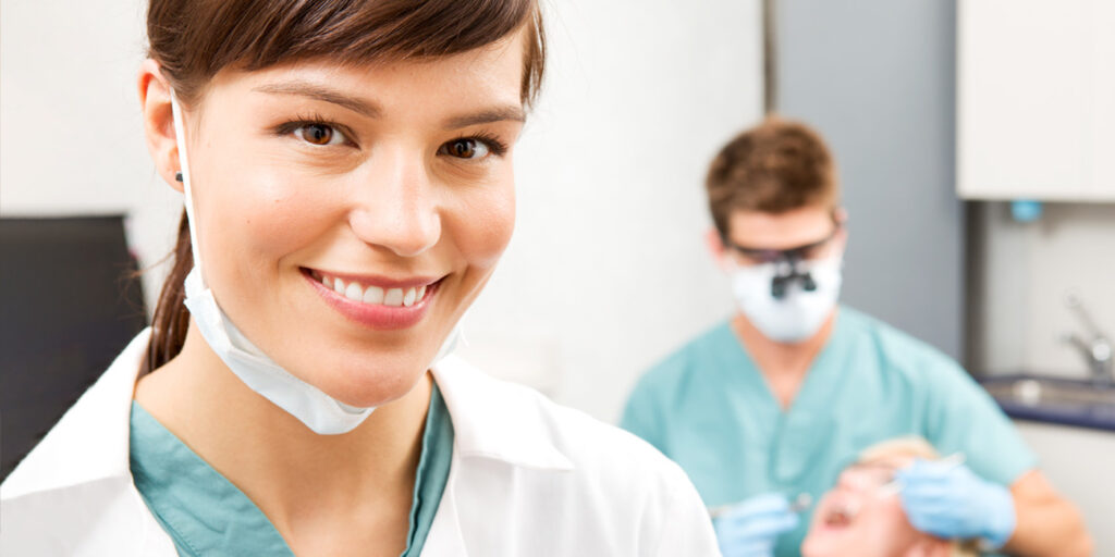Smiling female healthcare professional with colleague in background.