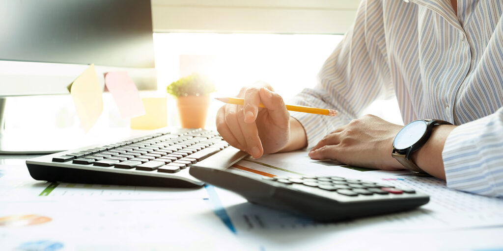 Person using calculator and writing notes at desk with keyboard nearby.